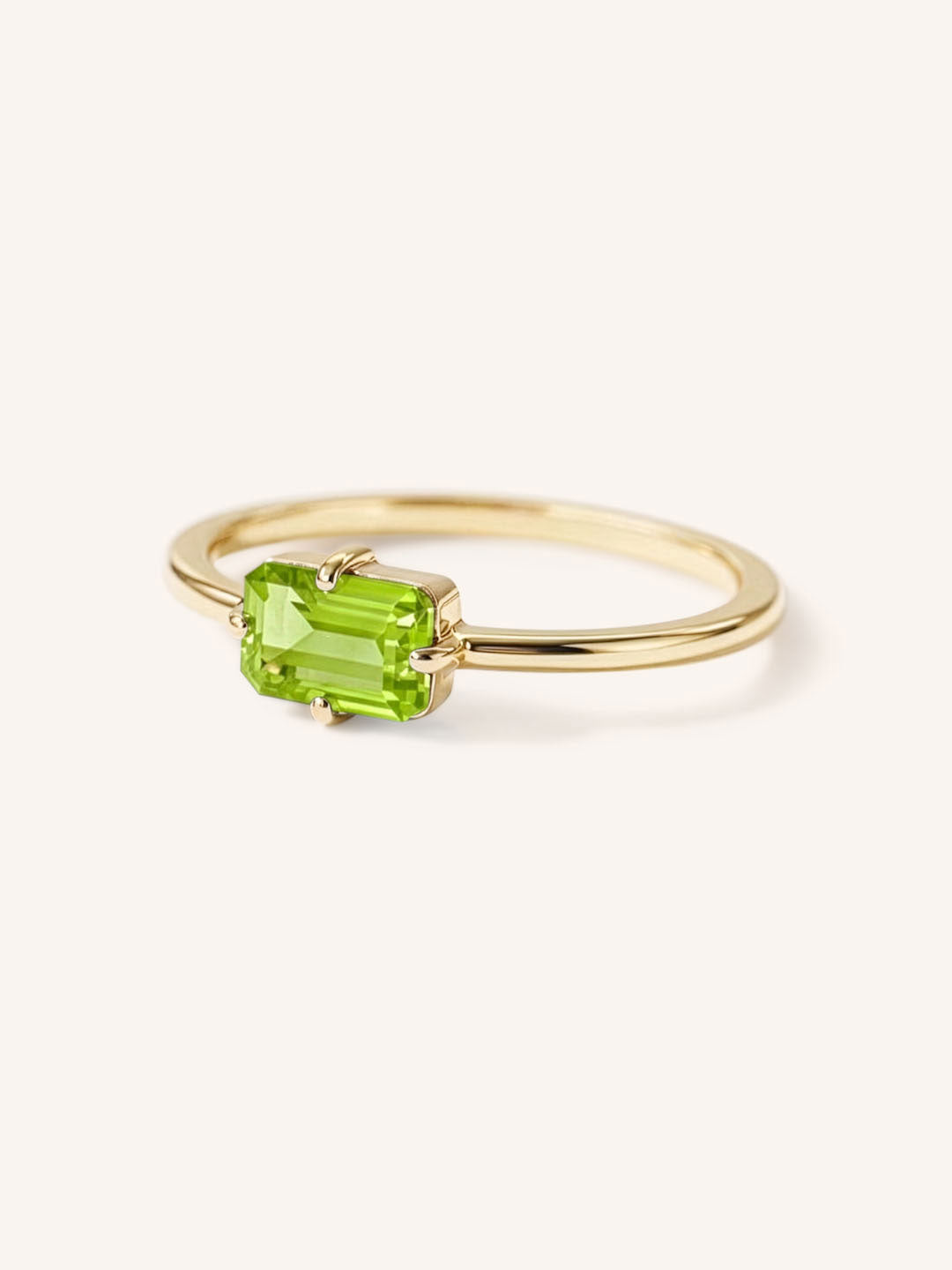 Yellow gold solitaire ring with emerald-cut peridot gemstone, side view on white background