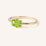 Yellow gold solitaire ring with emerald-cut peridot gemstone, side view on white background