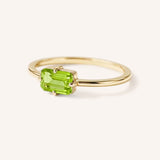 Yellow gold solitaire ring with emerald-cut peridot gemstone, side view on white background