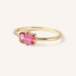 Yellow gold solitaire ring with emerald-cut pink tourmaline gemstone, side view on white background