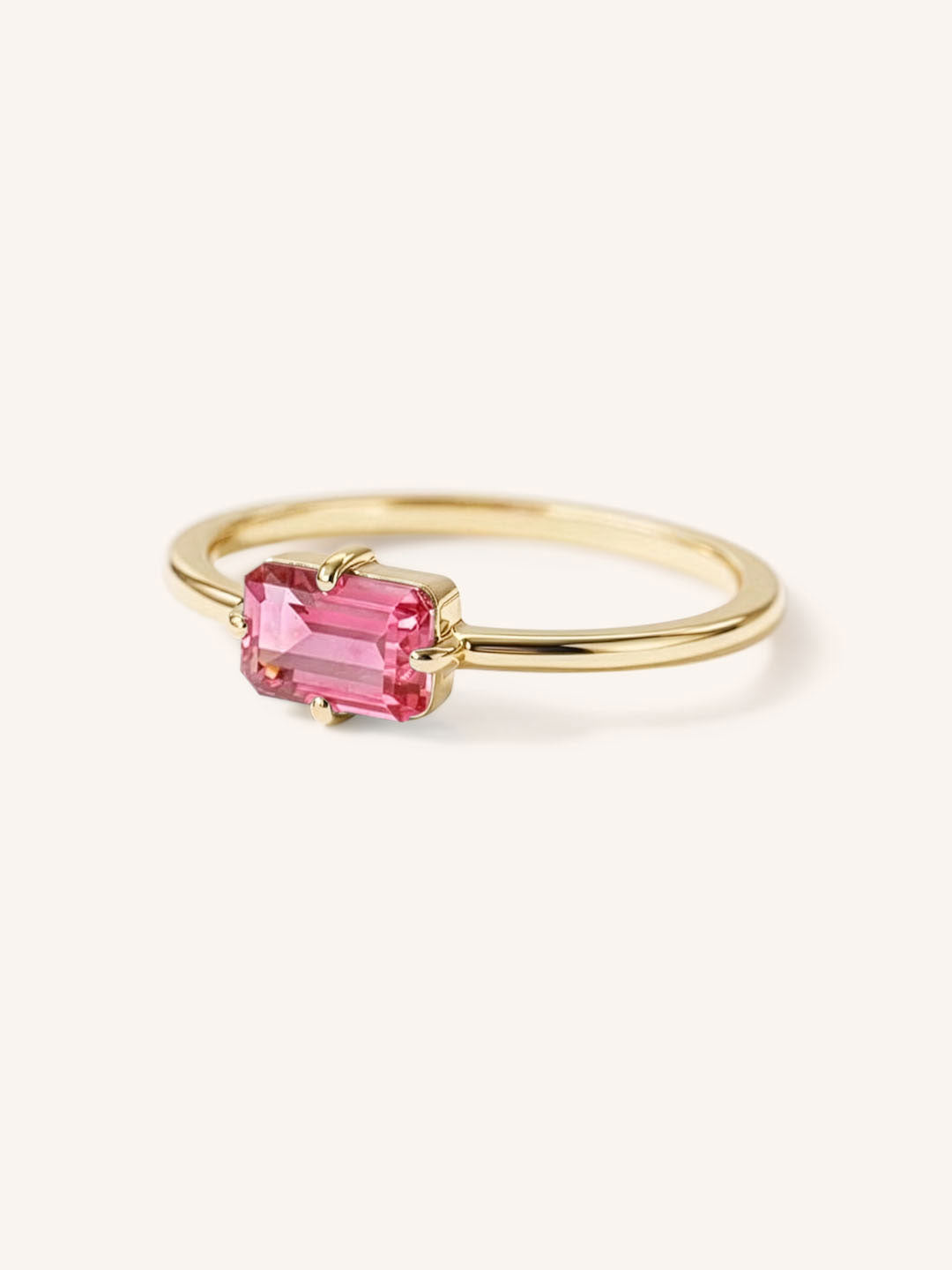 Yellow gold solitaire ring with emerald-cut pink tourmaline gemstone, side view on white background