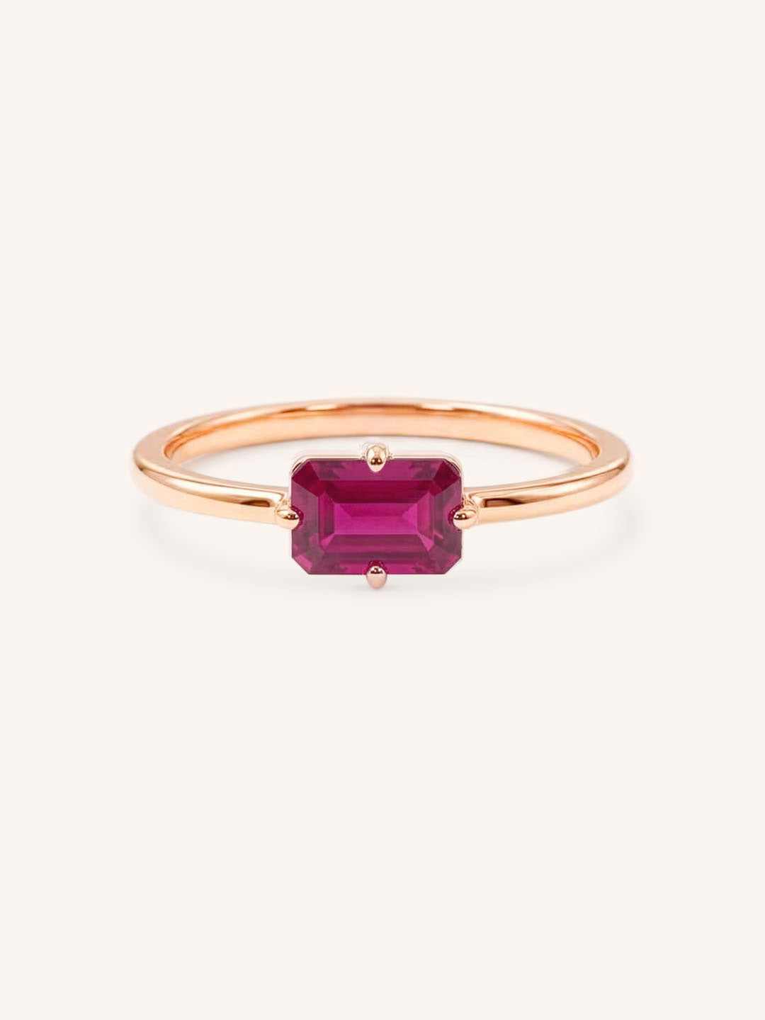 Rose gold solitaire ring with emerald-cut ruby gemstone on white background