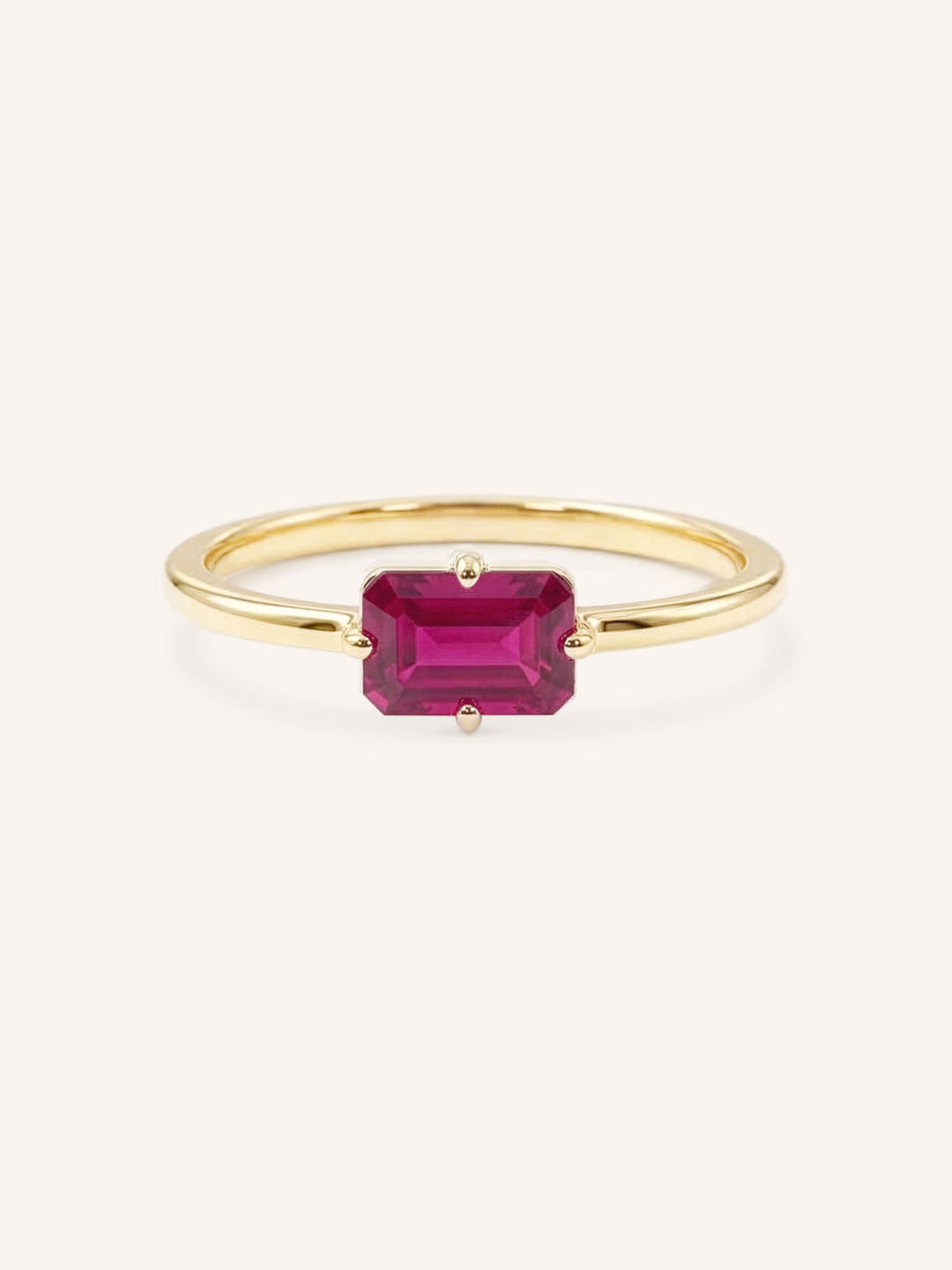 Yellow gold solitaire ring with emerald-cut ruby gemstone on white background