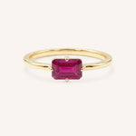 Yellow gold solitaire ring with emerald-cut ruby gemstone on white background