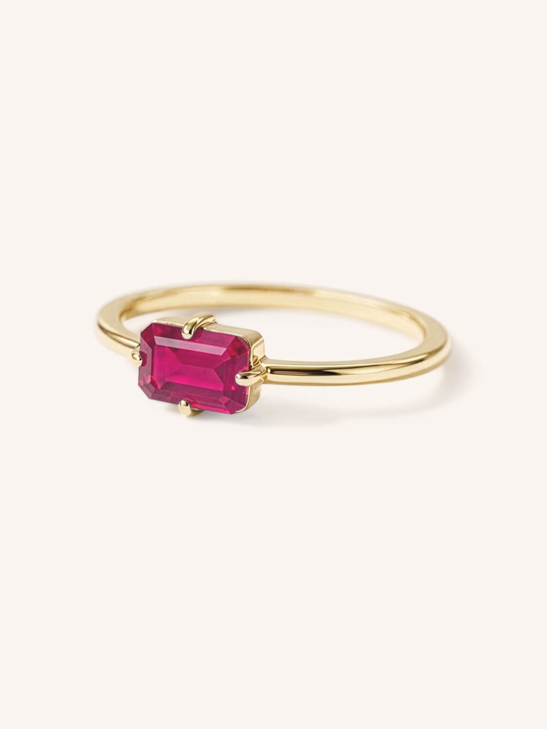 Yellow gold solitaire ring with emerald-cut ruby gemstone, side view on white background