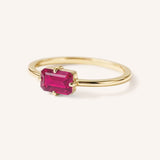 Yellow gold solitaire ring with emerald-cut ruby gemstone, side view on white background