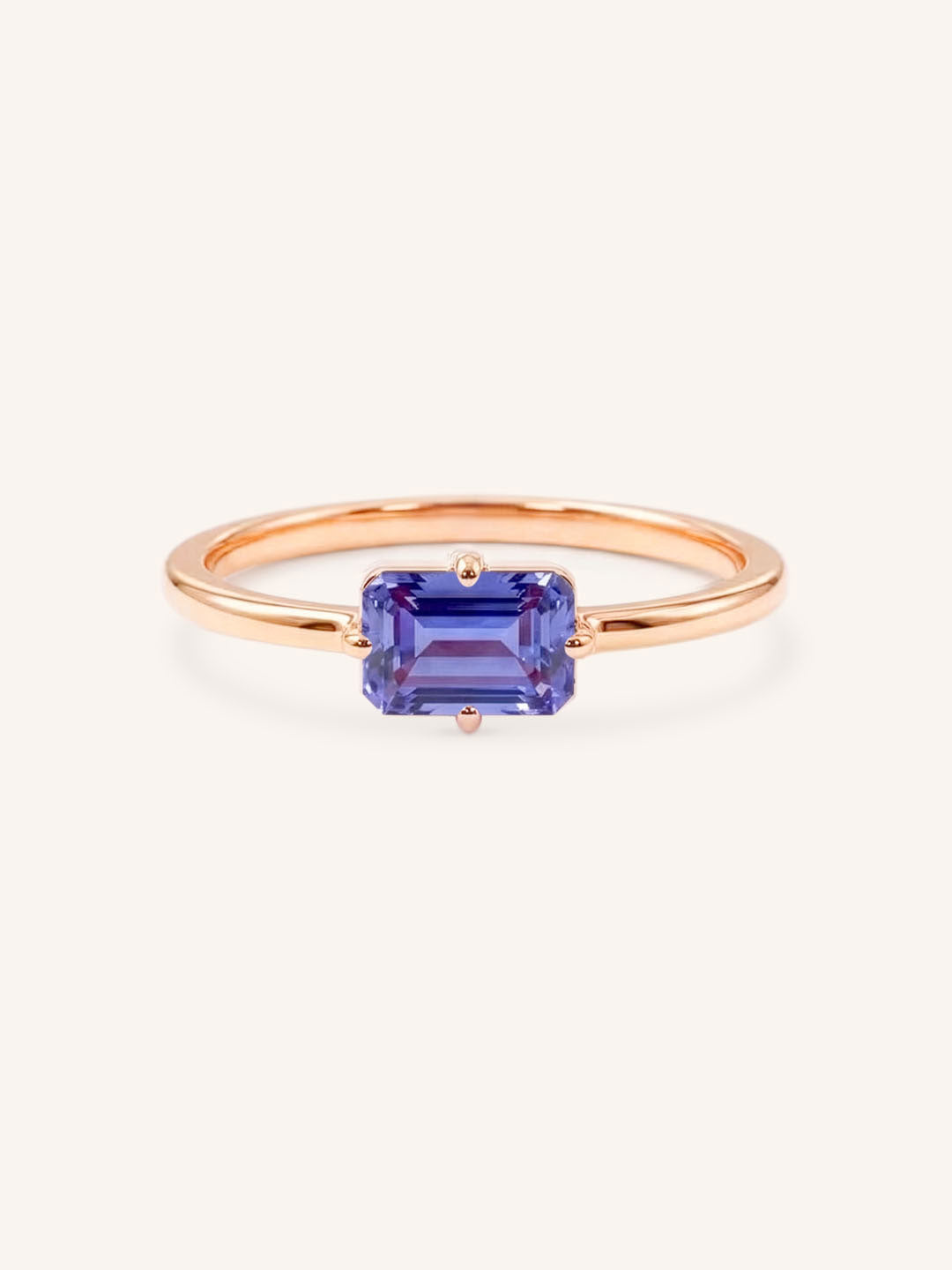Rose gold solitaire ring with emerald-cut tanzanite gemstone on white background
