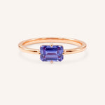 Rose gold solitaire ring with emerald-cut tanzanite gemstone on white background