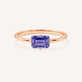 Rose gold solitaire ring with emerald-cut tanzanite gemstone on white background