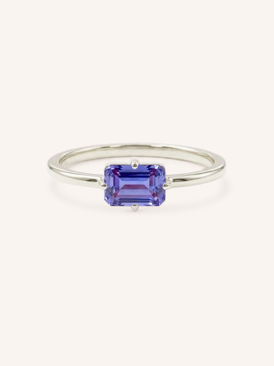 White gold solitaire ring with emerald-cut tanzanite gemstone on white background