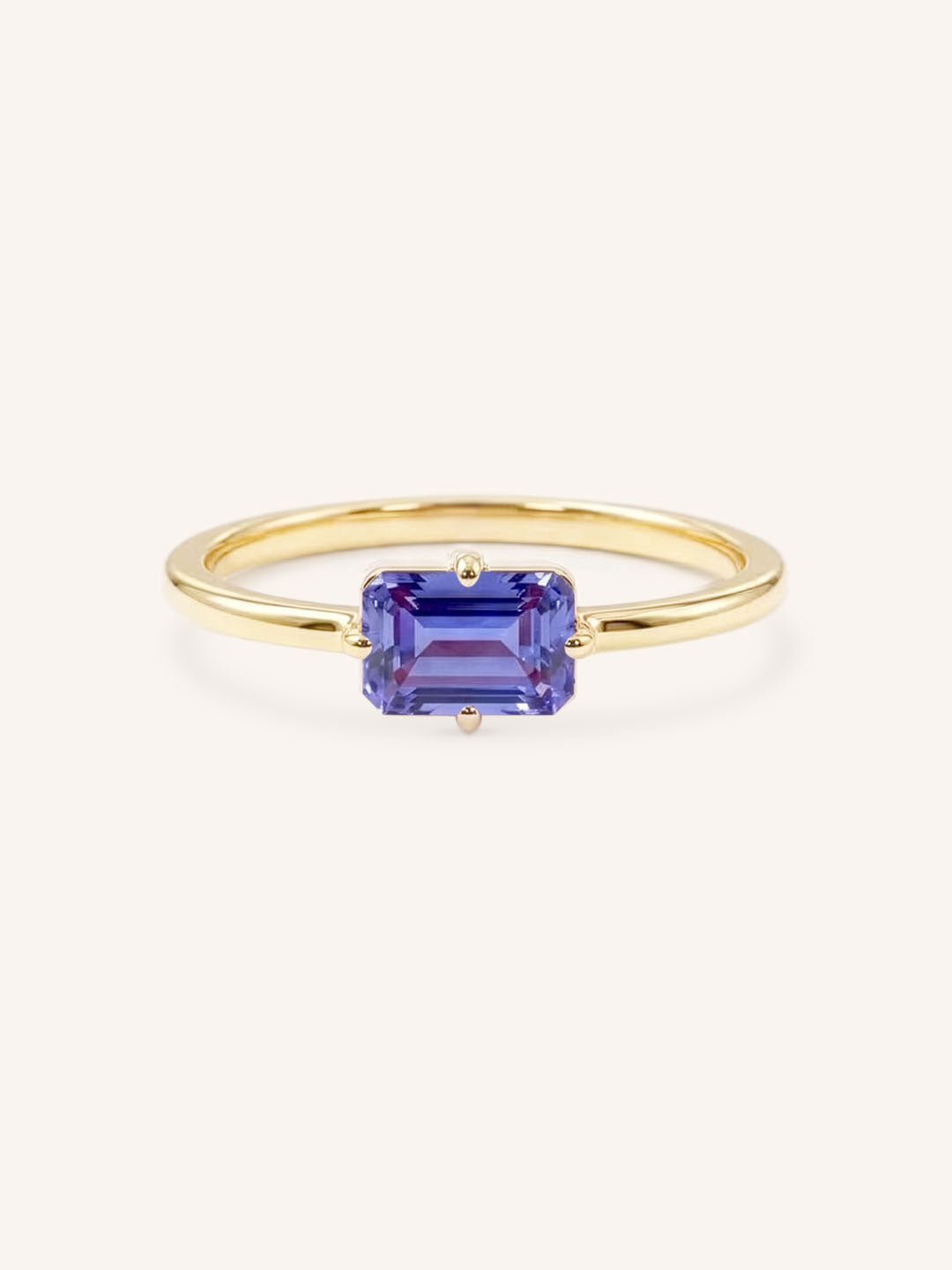 Yellow gold solitaire ring with emerald-cut tanzanite gemstone on white background