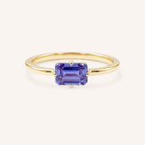 Yellow gold solitaire ring with emerald-cut tanzanite gemstone on white background
