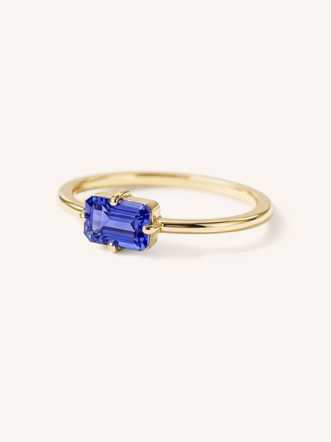 Yellow gold solitaire ring with emerald-cut tanzanite gemstone, side view on white background