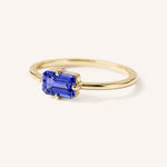 Yellow gold solitaire ring with emerald-cut tanzanite gemstone, side view on white background