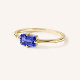 Yellow gold solitaire ring with emerald-cut tanzanite gemstone, side view on white background