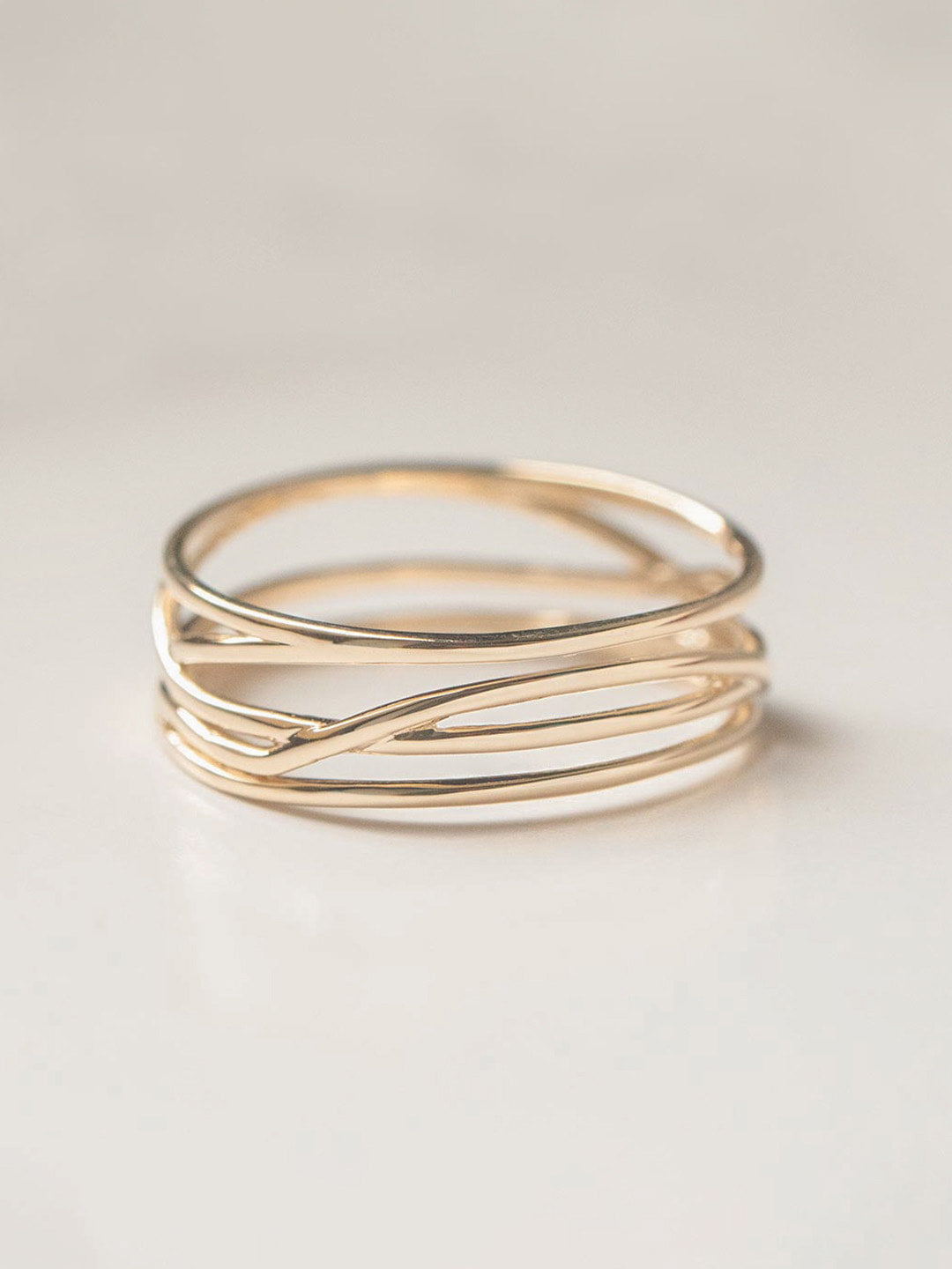 A twisted wide band gold ring with an entwined design, displayed against a neutral background.