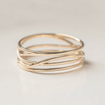 A twisted wide band gold ring with an entwined design, displayed against a neutral background.