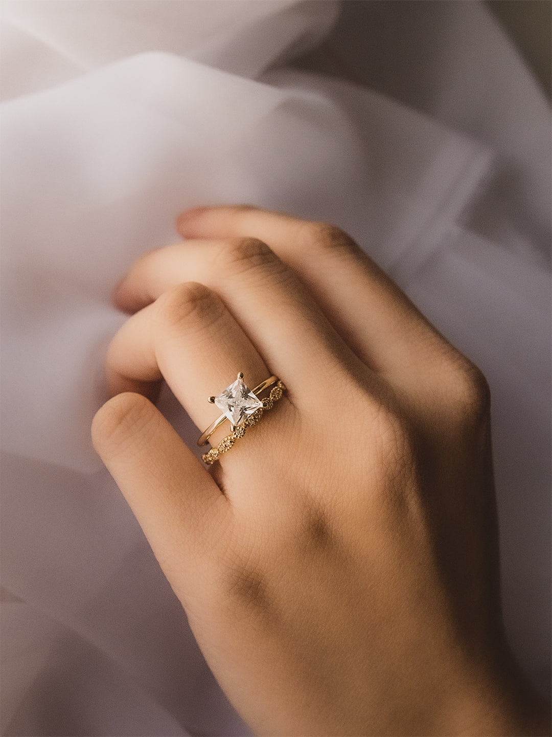 Gold princess cut diamond engagement ring with diamond wedding band worn on hand