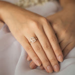 Close-up of a hand wearing a ring with an Emerald Cut morganite and a halo of small diamonds with a soft background