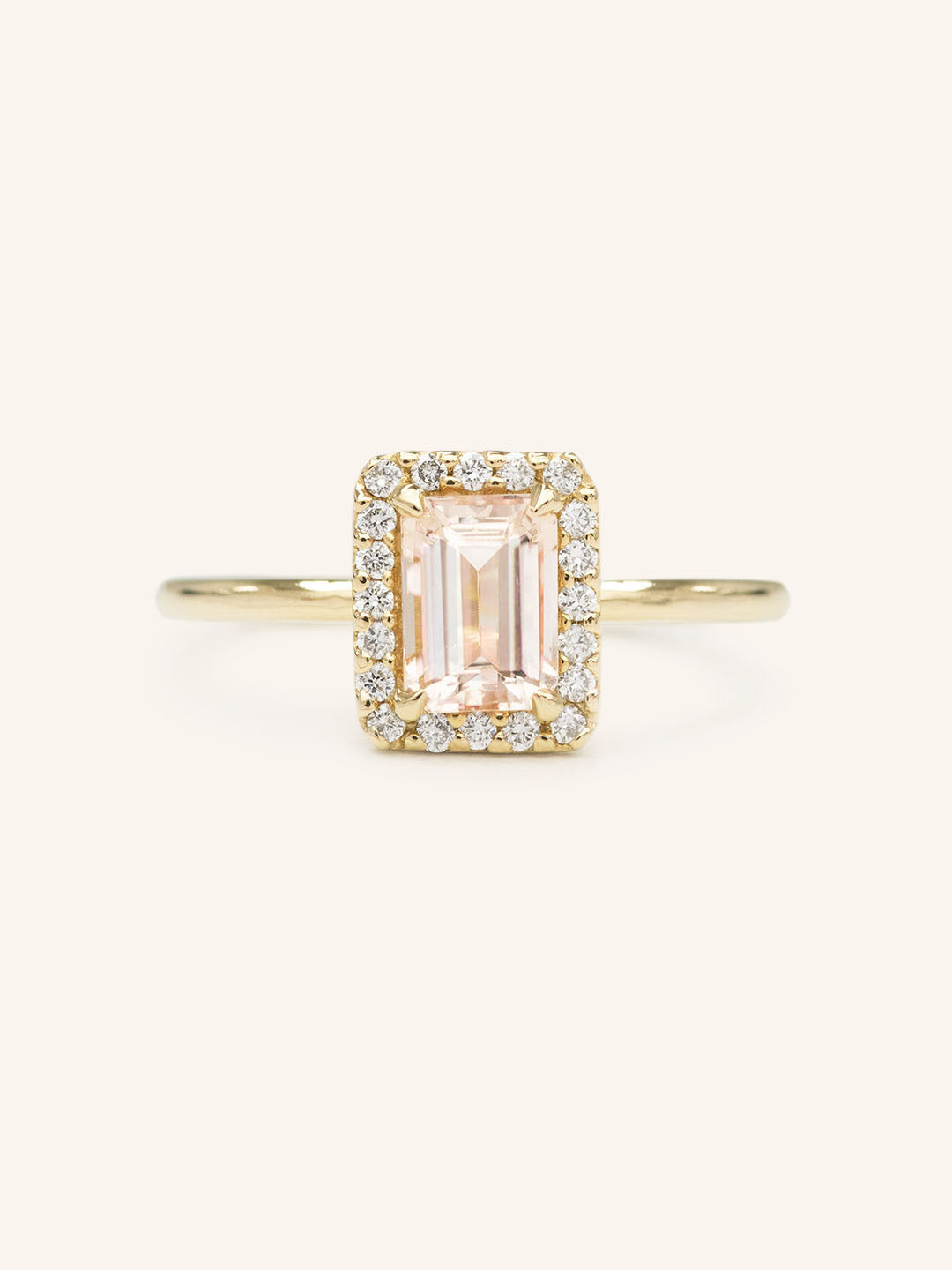A engagement ring with a central morganite gemstone, surrounded by a halo of smaller clear stones set in a gold band.