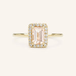 A engagement ring with a central morganite gemstone, surrounded by a halo of smaller clear stones set in a gold band.