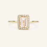 A engagement ring with a central morganite gemstone, surrounded by a halo of smaller clear stones set in a gold band.