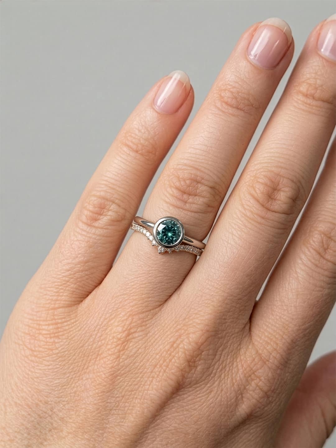 Hand wearing hidden bezel Montana sapphire engagement ring with curved diamond band on neutral background
