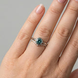 Hand wearing hidden bezel Montana sapphire engagement ring with curved diamond band on neutral background