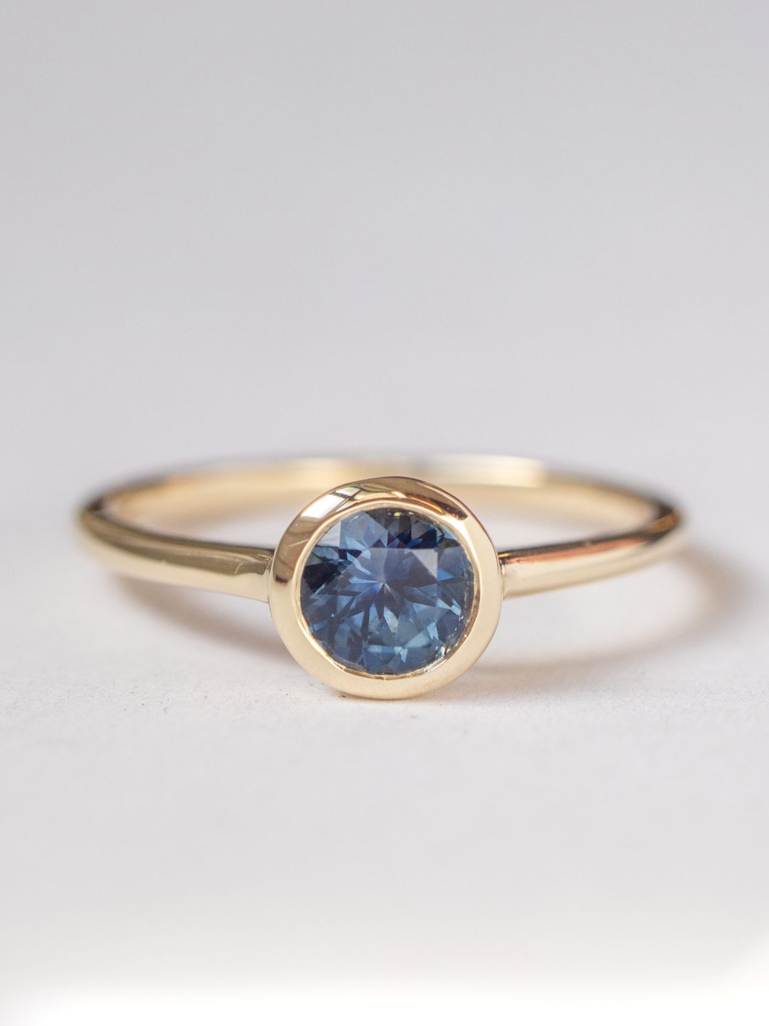 A gold band engagement ring with a round deep blue-green montana sapphire centerpiece, set in a sleek bezel encapsulation.