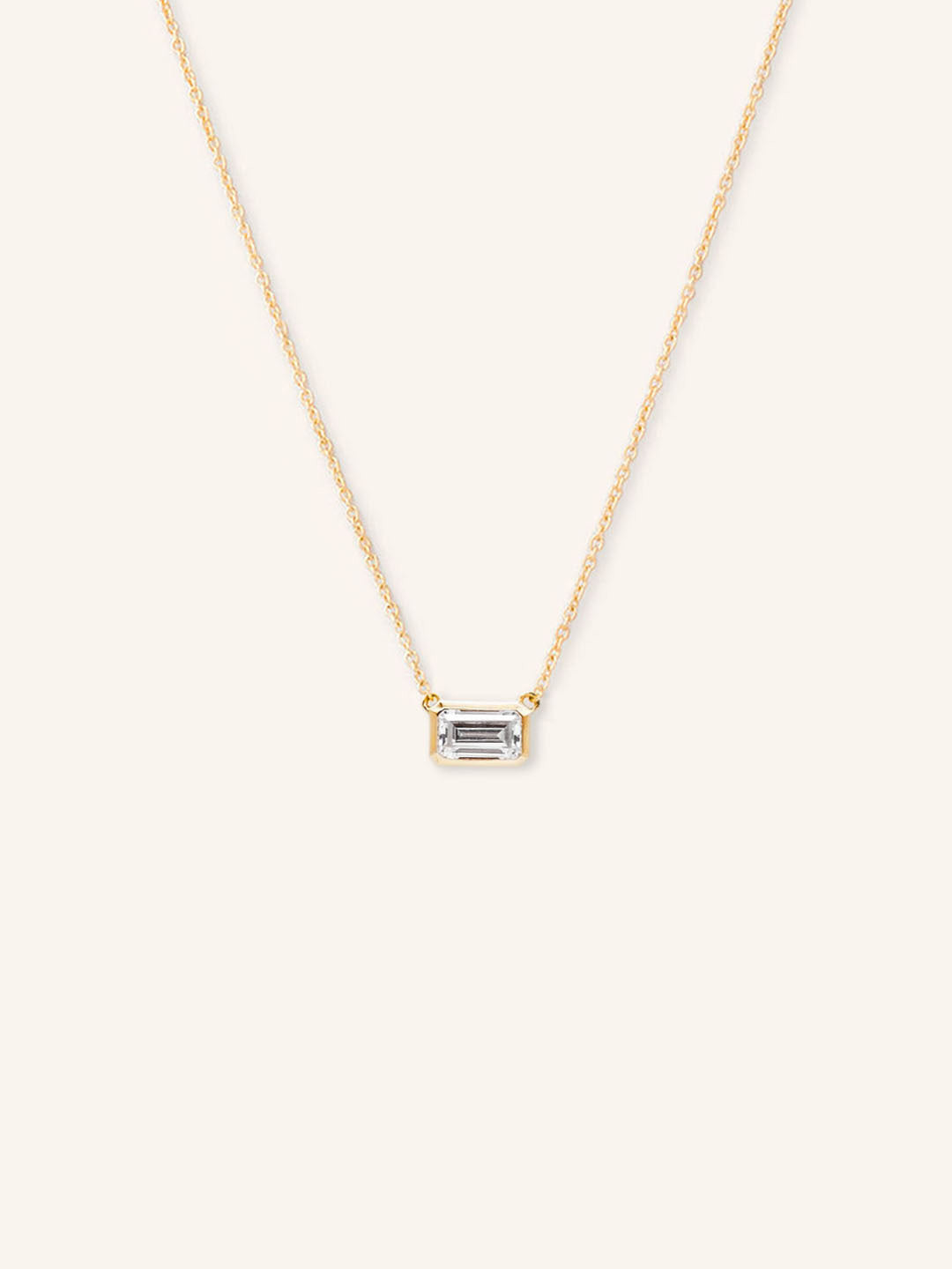A gold-colored bezel necklace with a central emerald-cut moissanite gemstone.