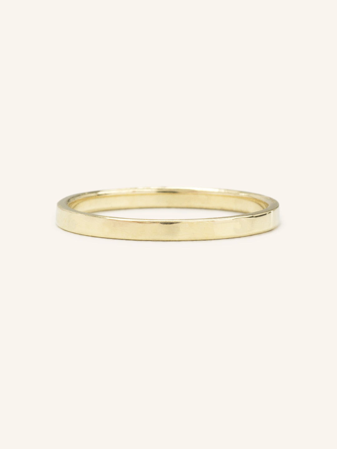 A flat, 2MM wide, gold wedding band on a plain background.